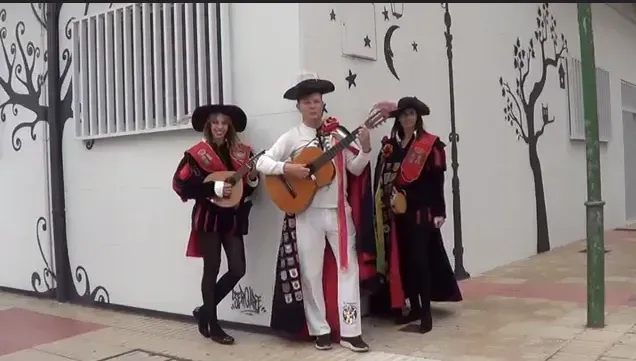 Tres personas con trajes tradicionales tocando instrumentos de cuerda fuera de un edificio.
