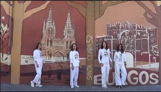 Cuatro mujeres vestidas de blanco posan delante de un mural que representa una ciudad con una catedral y BURGOS pintado en la pared.