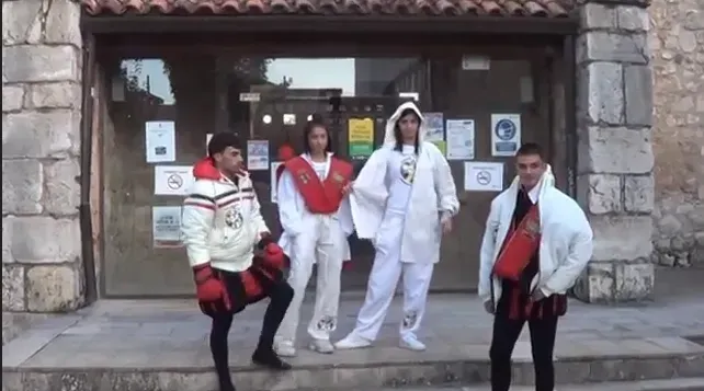Cuatro personas posando fuera del edificio. Una con chaleco rojo y pantalón negro, otra con equipo blanco de taekwondo y dos con capuchas blancas.