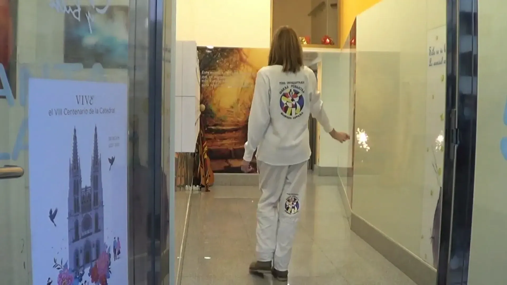 Una persona con uniforme blanco camina por un pasillo bien iluminado y abre una puerta de vidrio.