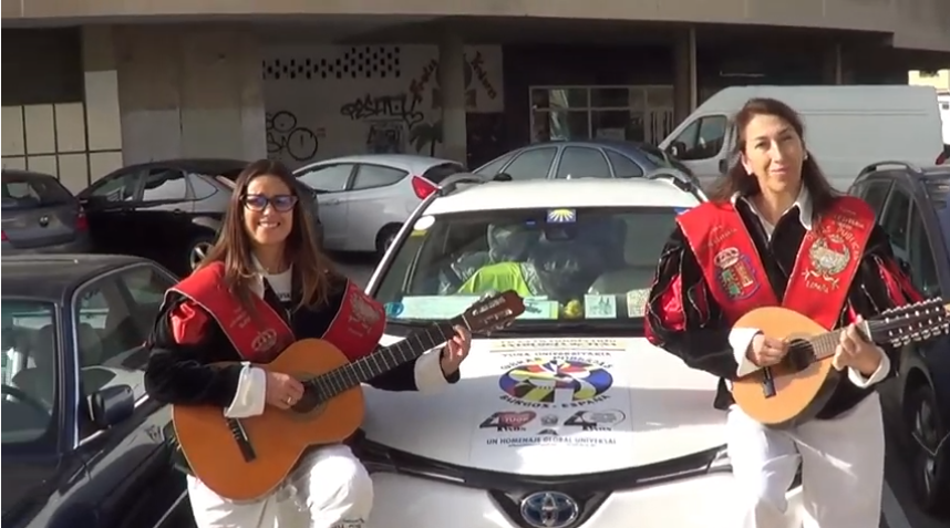 Dos mujeres vestidas académicamente tocan la guitarra y la mandolina delante de un coche.