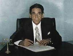 Hombre de traje escribiendo en un escritorio. Balanza de plata sobre el escritorio.