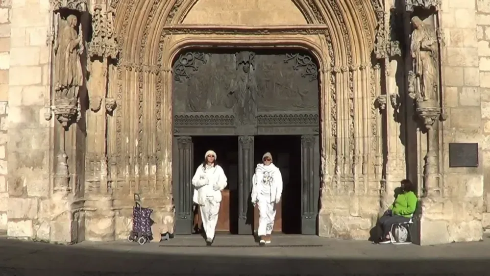 Dos personas vestidas de blanco salen de una gran puerta ornamentada; una persona se sienta a la derecha.