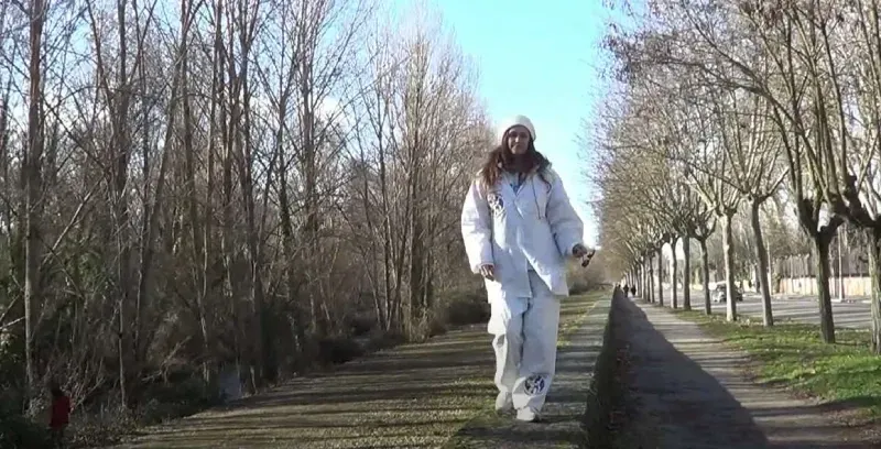 Una mujer con traje blanco de invierno camina por un sendero entre árboles. Día soleado.