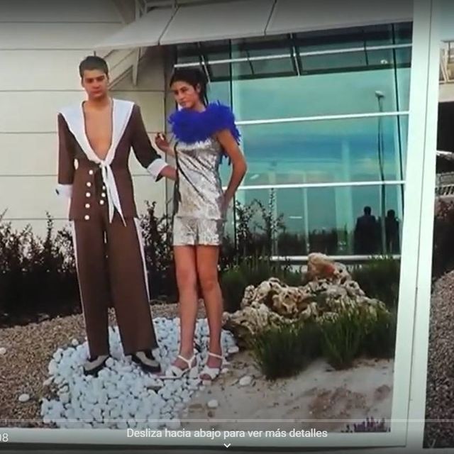 Hombre con traje marrón y mujer con vestido plateado posando al aire libre.