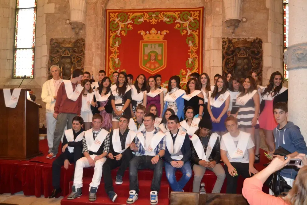 Grupo de graduados con vestimenta formal, posando en un entorno similar a una iglesia con un escudo.