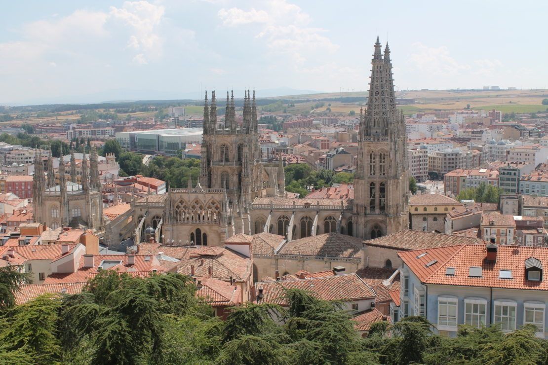 La Catedral de Burgos, España, se eleva sobre tejados de tejas rojas y el paisaje urbano en un día soleado.
