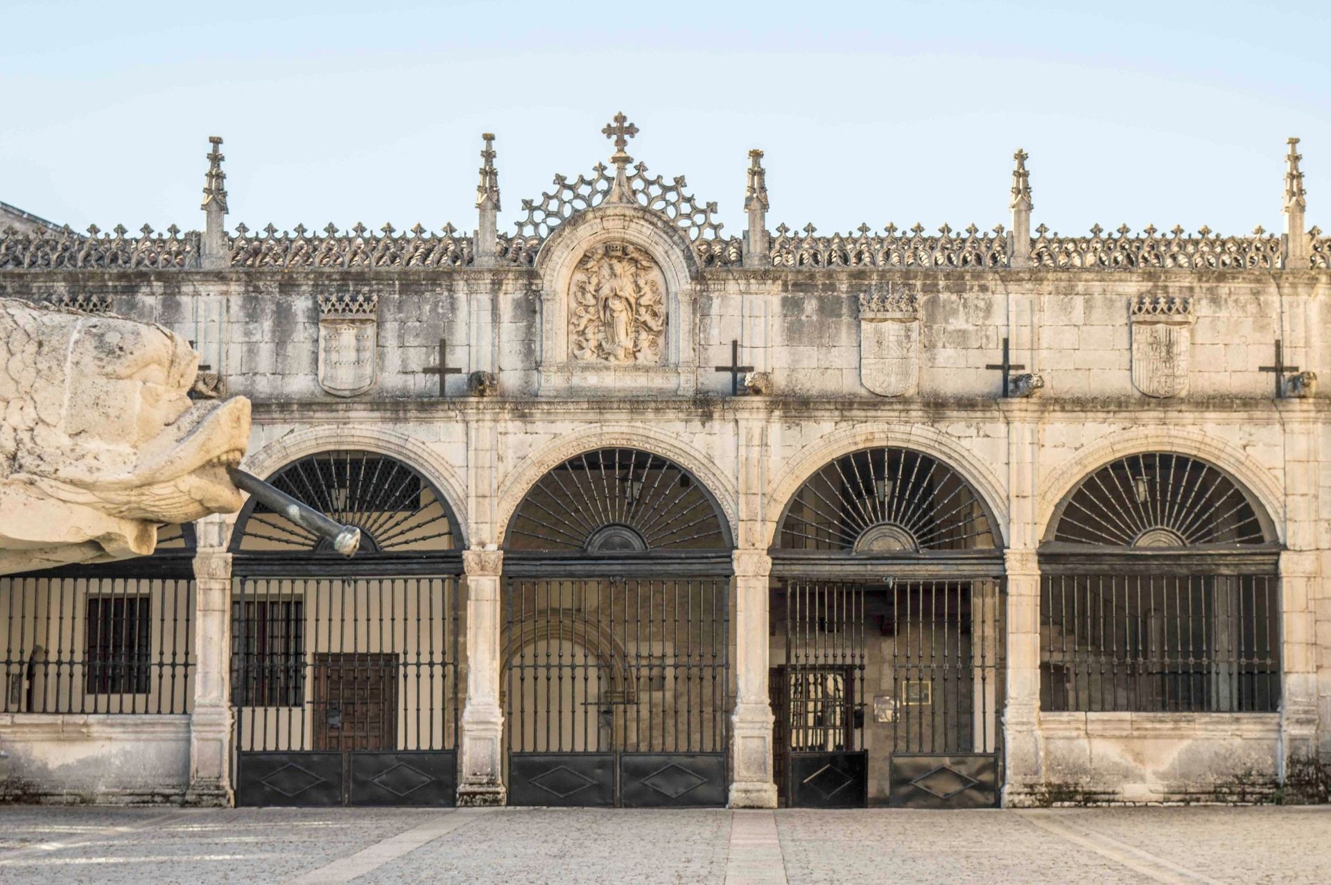 Exterior de un edificio histórico de piedra con entradas arqueadas, puertas de hierro y agujas decorativas.