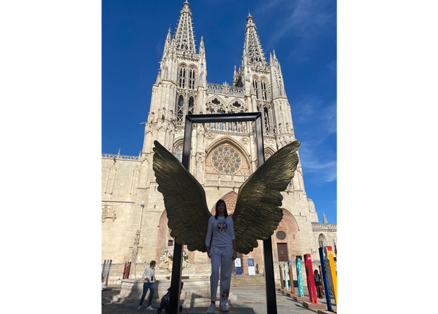 Mujer posa con escultura de alas de ángel doradas frente a la Catedral de Burgos, España.