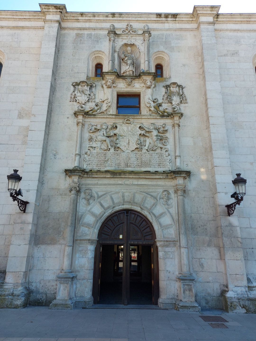 Fachada de edificio de piedra con puerta arqueada, tallas ornamentadas y puertas de madera abiertas.