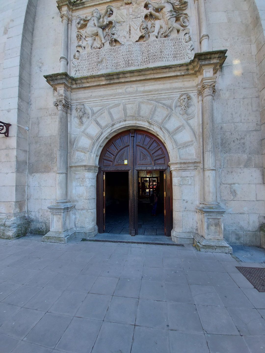 Entrada arqueada de piedra de un edificio con puertas de madera abiertas. La luz brillante entra desde el interior.