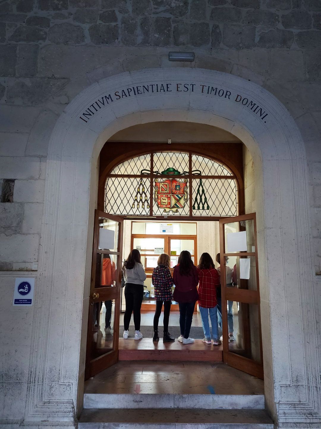 Cuatro jóvenes se encuentran en la entrada de un edificio con un arco de piedra.