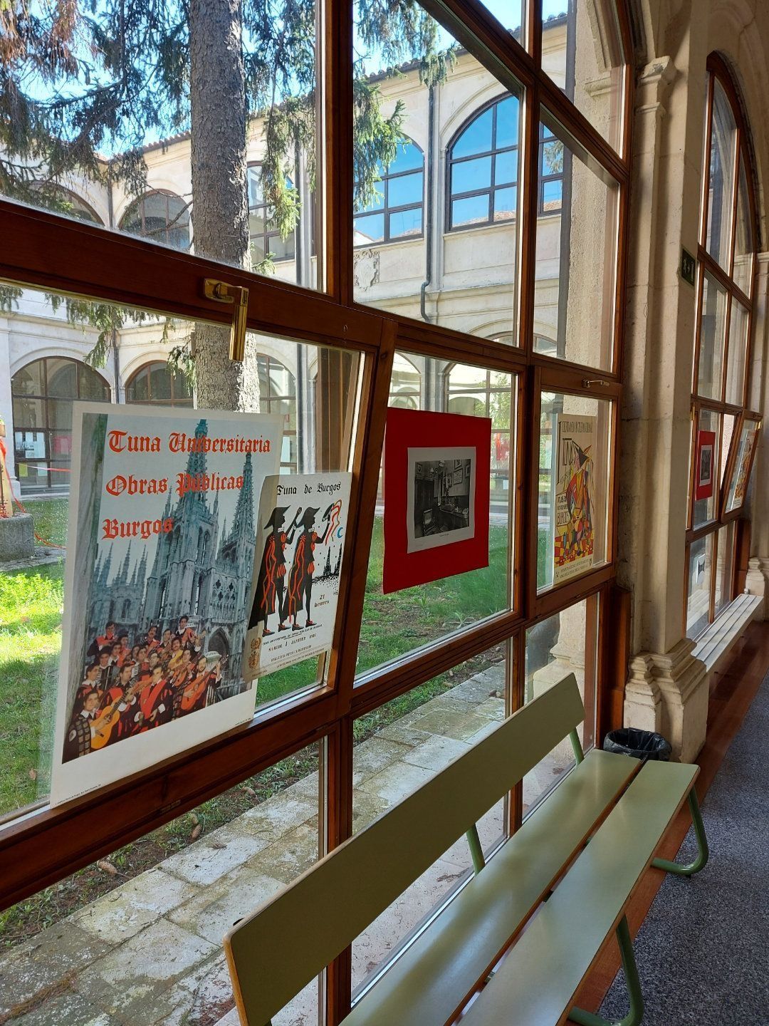 Vista a través de una ventana con carteles. La luz del sol ilumina un banco y el patio de un edificio.