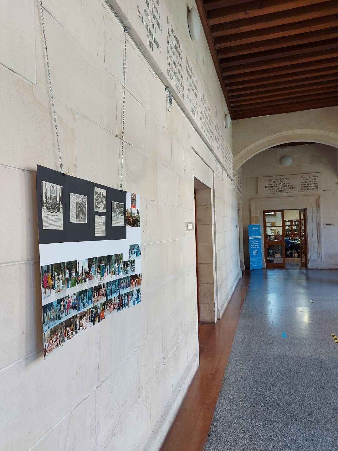 Exhibición de fotografías en la pared de un pasillo. Techo marrón, paredes color canela, suelo rojo.