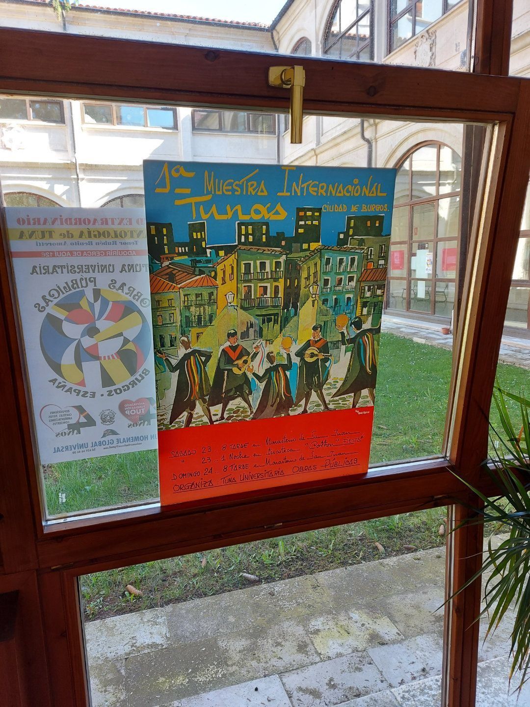 Carteles en la ventana: anuncio teatral vintage, ilustración colorida de personas, escenario de patio al aire libre.