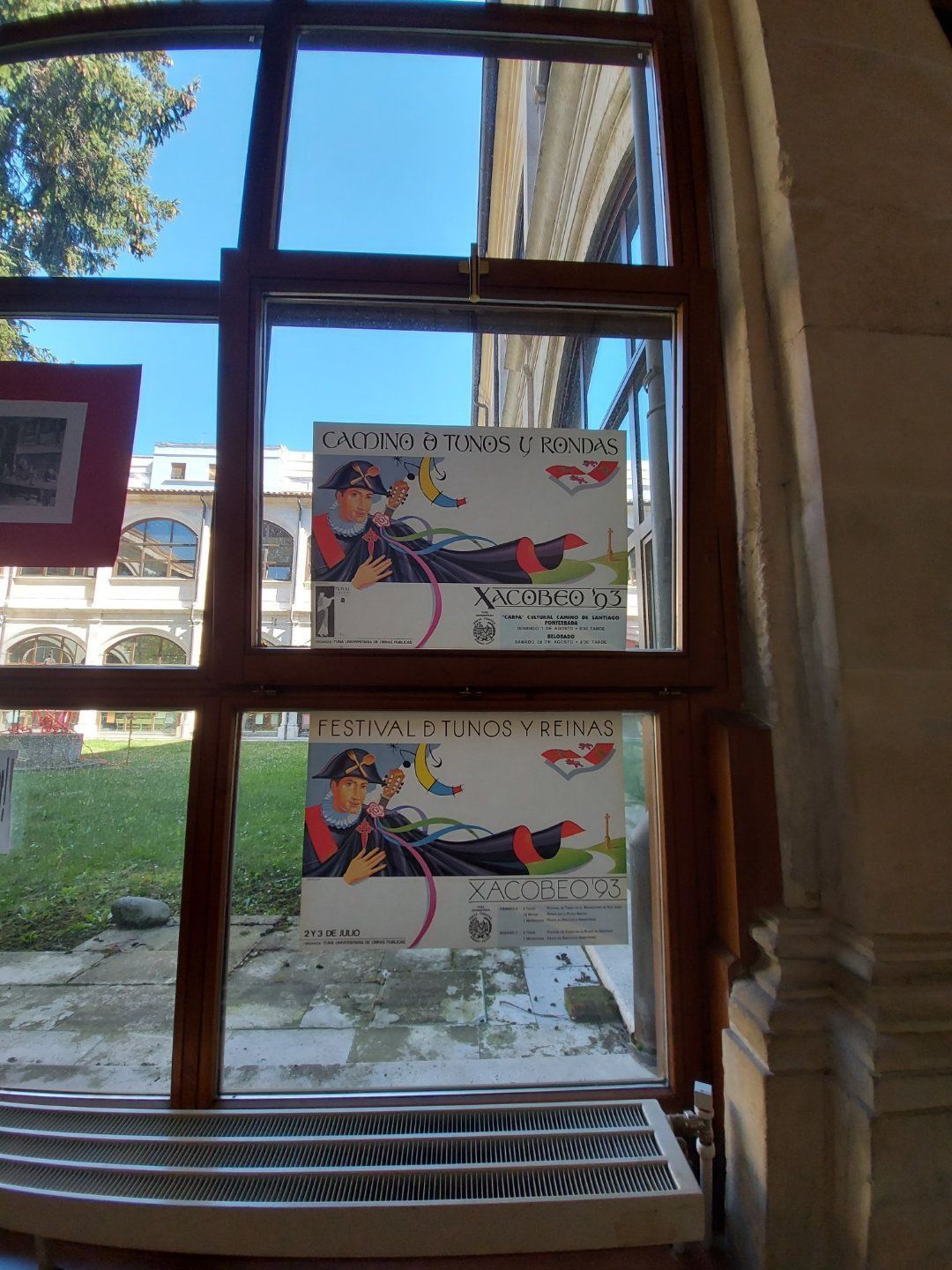 Ventana con dos carteles antiguos de una figura enmascarada, vistos desde dentro. Exterior: césped verde, día soleado.