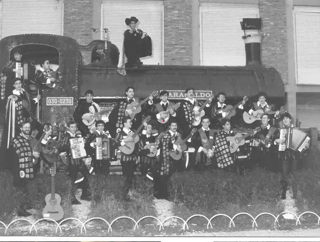 Músicos disfrazados tocan instrumentos sobre una carroza de tren. Foto en blanco y negro.