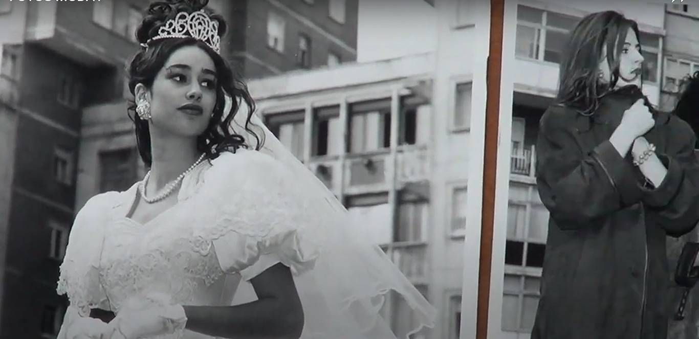 Una mujer con vestido de novia mira por encima del hombro, otra mujer está parada cerca, ambas en escala de grises.