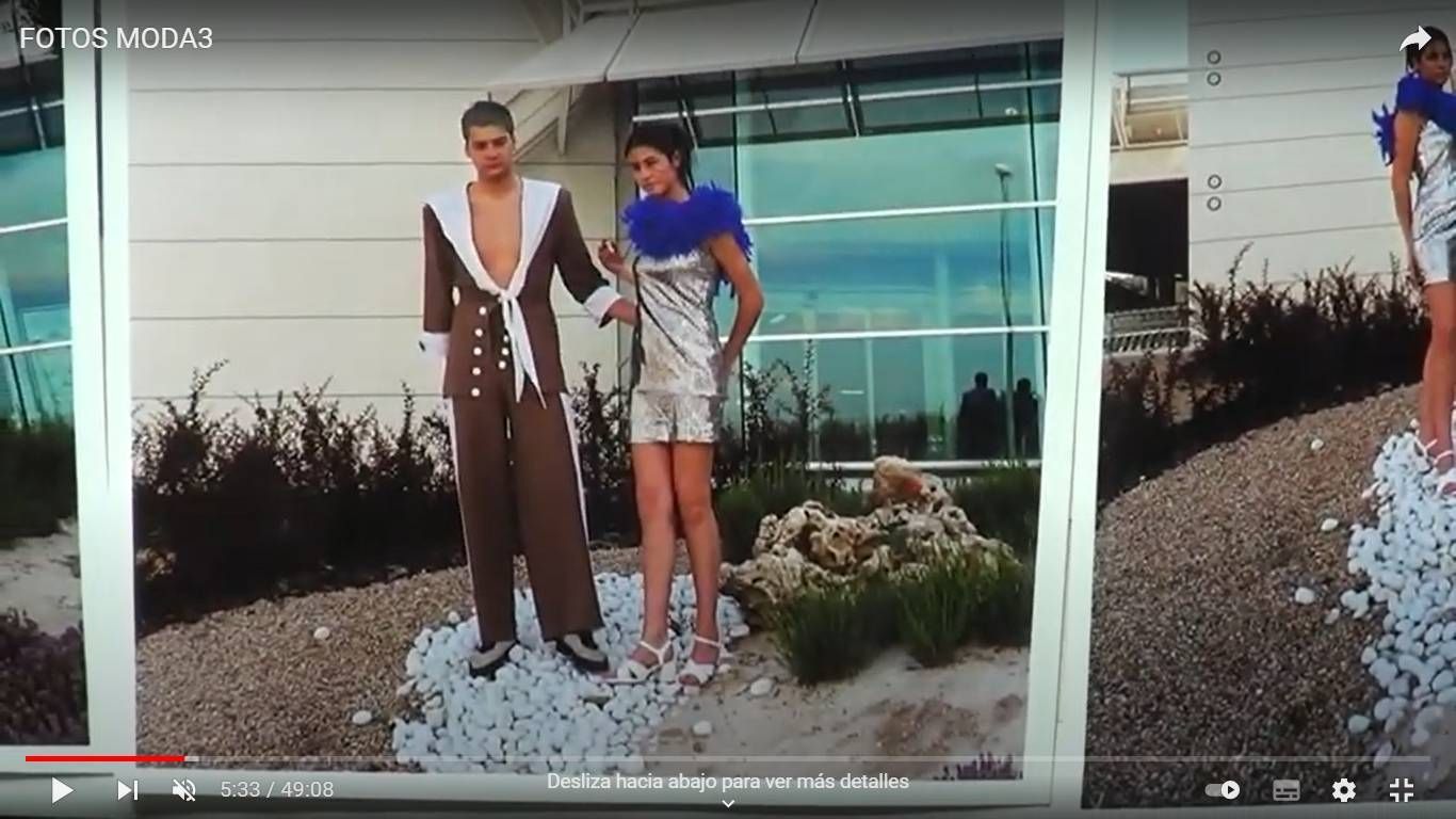 Dos modelos de moda posando al aire libre frente a un edificio, un hombre con traje marrón y una mujer con un vestido plateado.