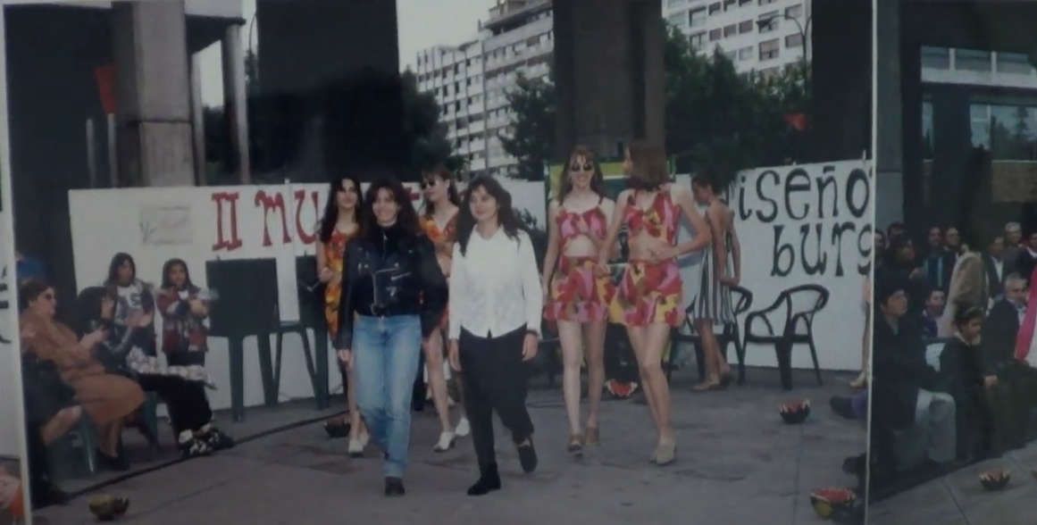 Desfile de moda al aire libre: modelos con coloridos minivestidos desfilan. El público observa a dos mujeres que encabezan el desfile.