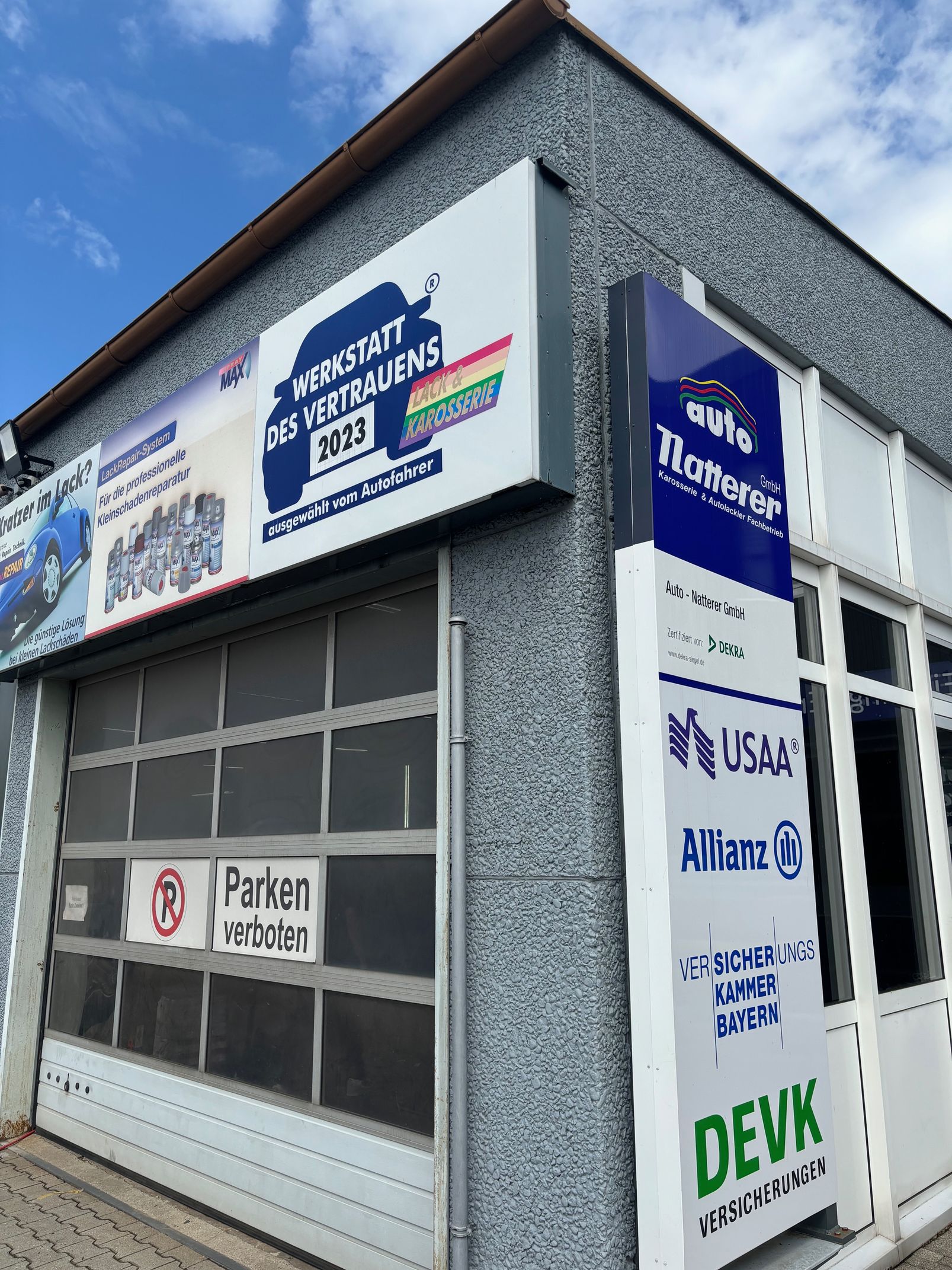 Ein Eckgebäude mit Garagentor und mehreren Schildern, darunter „Aladin Serviceteam“ und „Zilmerer“.