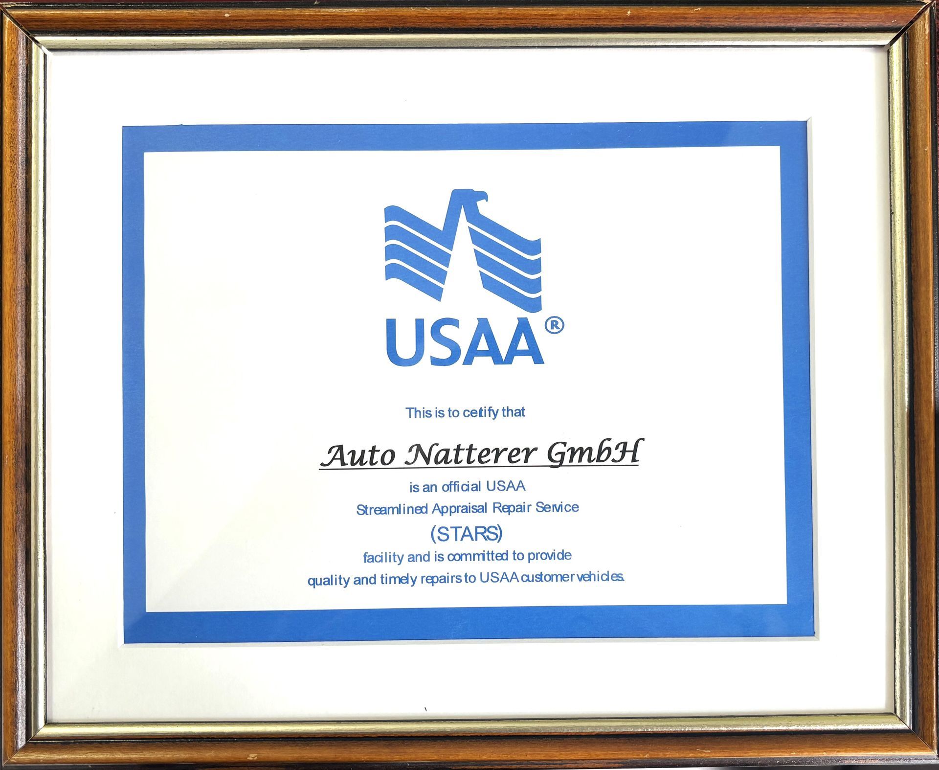 Gerahmtes USAA-Zertifikat für Auto Natterer GmbH, mit blauem Logo auf weißem Hintergrund, gerahmt in braunem Holz.