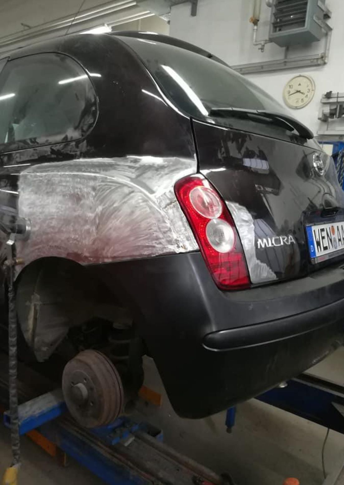 Schwarzer Nissan Micra in einer Reparaturwerkstatt, Karosserie teilweise repariert und grundiert.