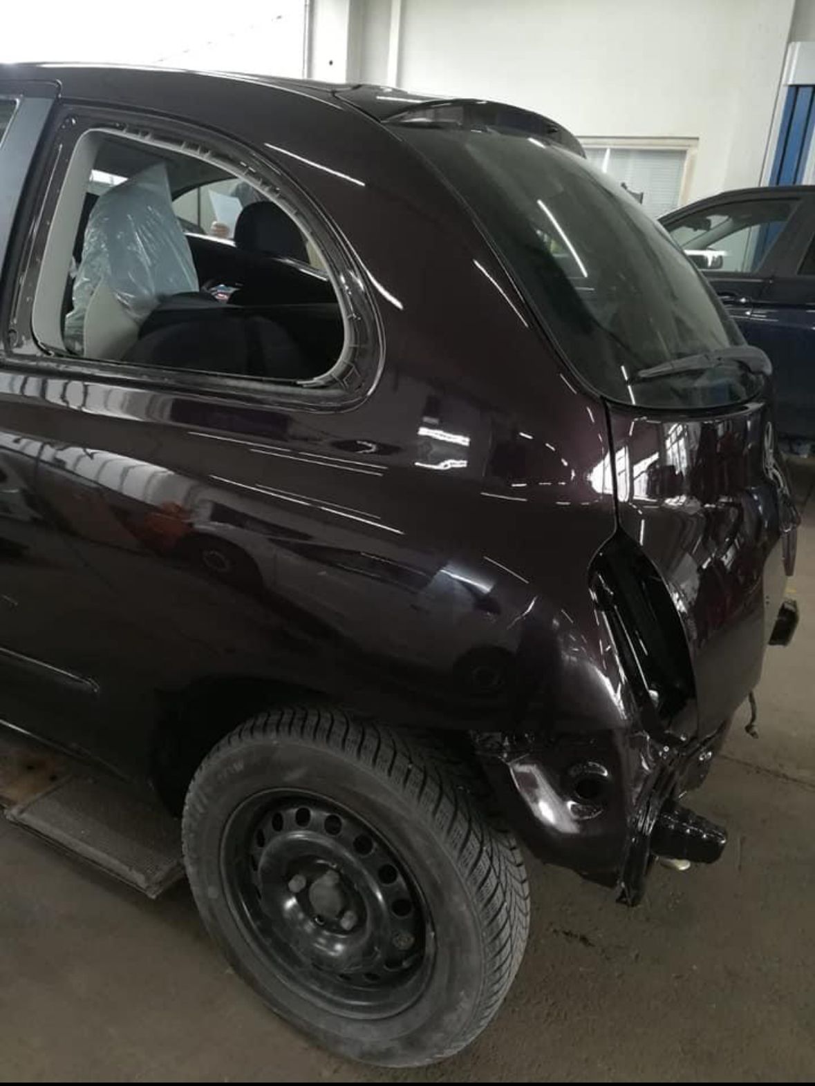 Dunkelbraunes Fließheckauto ohne Rücklicht und Stoßstange in einer Reparaturwerkstatt.