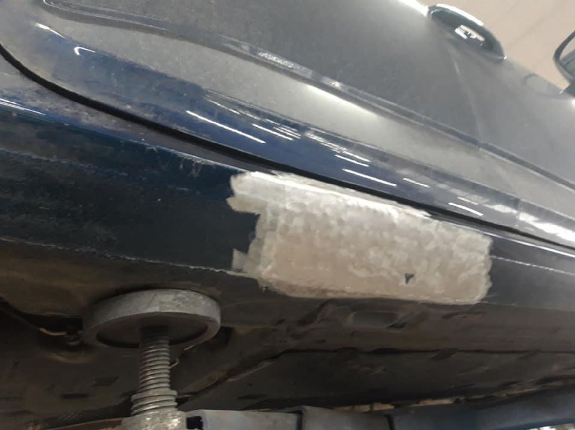 Blaue Autoseite mit einem Flicken Reparaturmaterial in der Nähe der Unterseite. Wagenheber unter dem Auto.