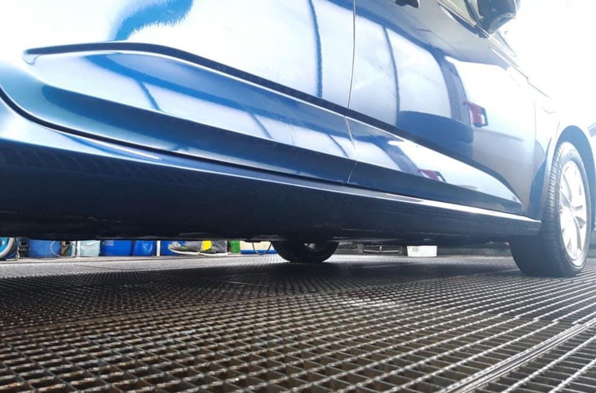 Seitenansicht eines blauen Autos auf einem Metallgitter, das Licht reflektiert.