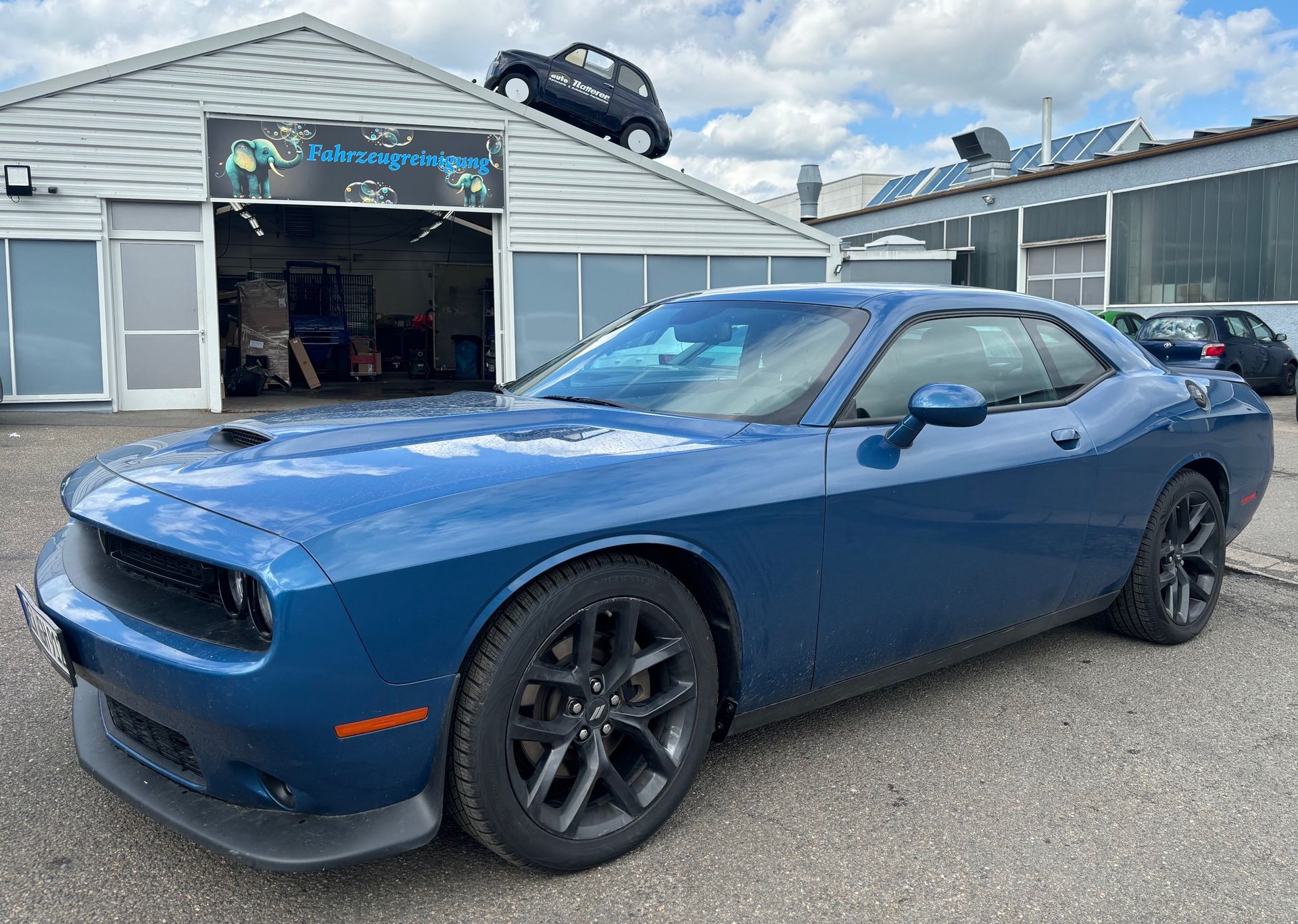 Blauer Dodge Challenger vor einer Autowaschanlage, Kleinwagen auf dem Dach.