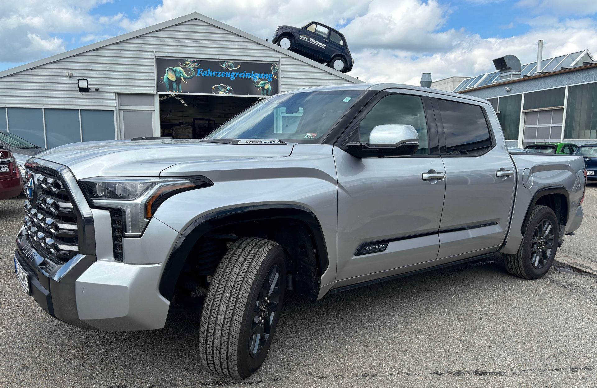 Vor einem Gebäude parkender silberner Toyota Tundra-Truck, auf dem ein Kleinwagen thront.