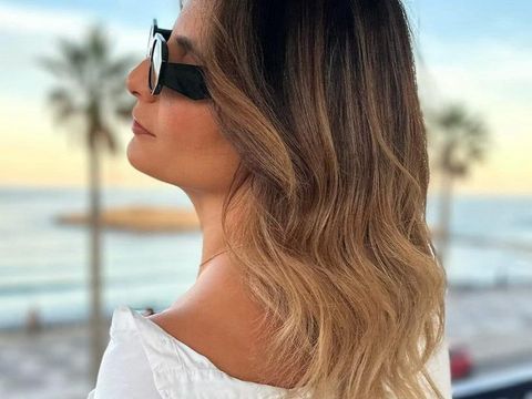 Femme avec un balayage blond de profil face à la mer avec des lunettes de soleil