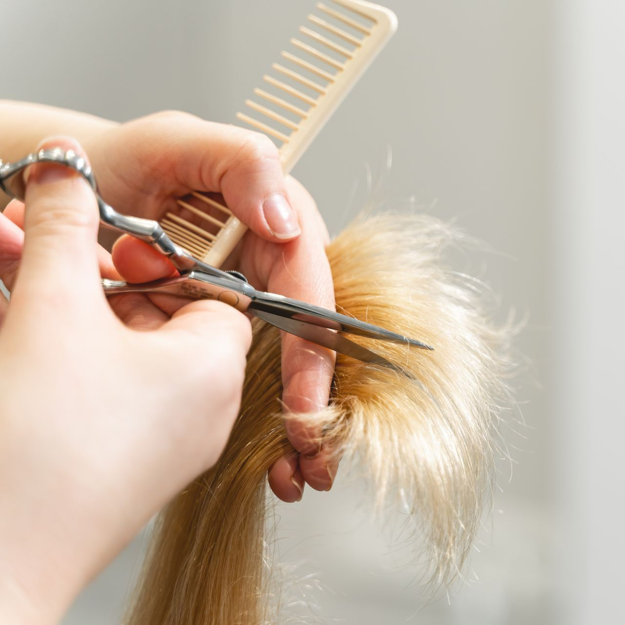 Zoom sur une personne qui coupe les pointes de cheveux blonds