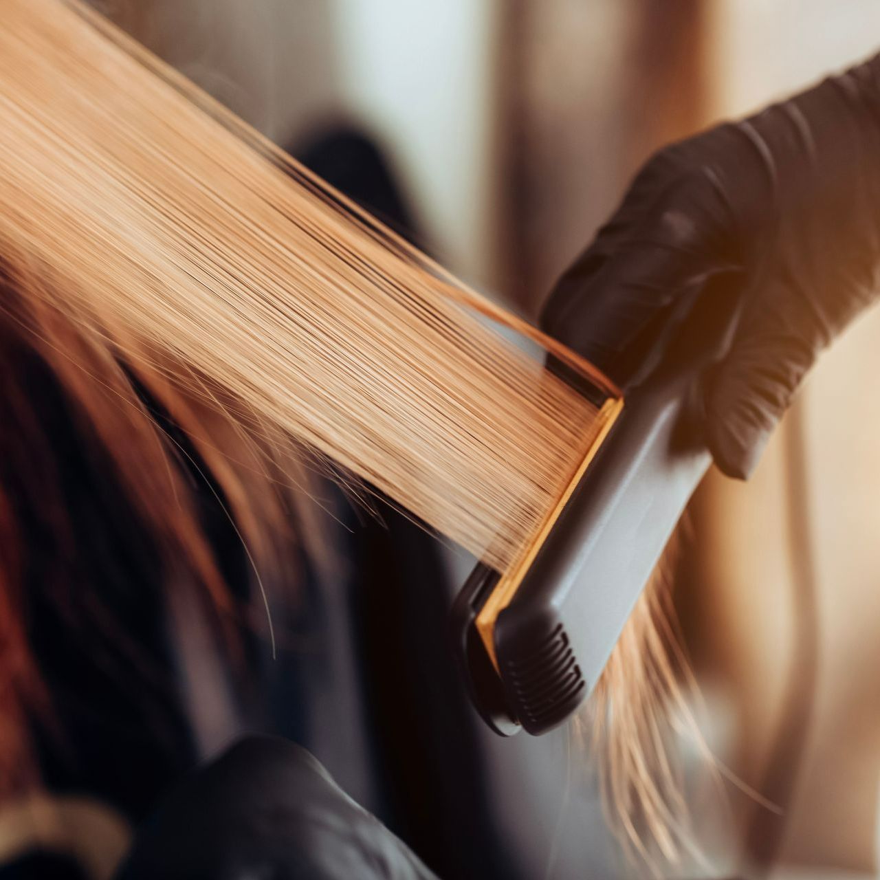 Personne qui lisse des cheveux avec des gants et un lisseur noir