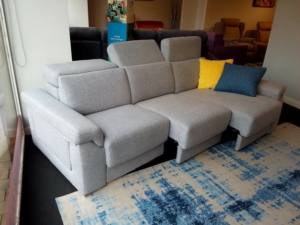 Sofá seccional moderno de color gris claro con cojines coloridos en una sala de estar, junto a una alfombra azul y blanca.