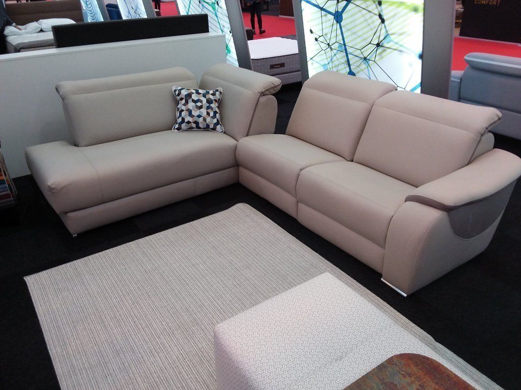 Sala de estar moderna con sofás seccionales de color beige, una alfombra estampada y un pequeño puf.