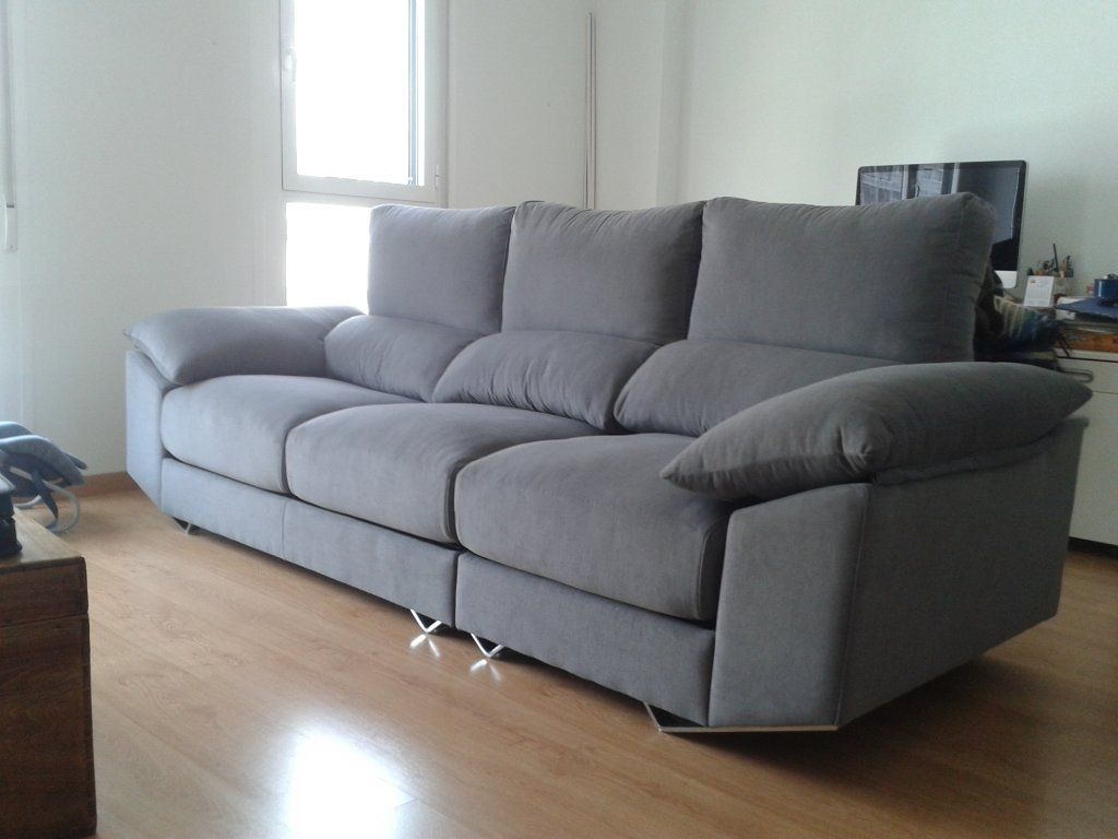 Sofá seccional gris en una habitación luminosa con suelo de madera y una ventana cercana.