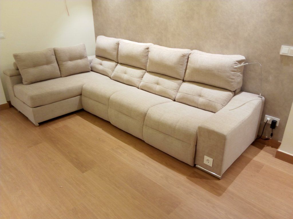 Sofá modular de color beige en una habitación pequeña con suelo de madera y paredes lisas.