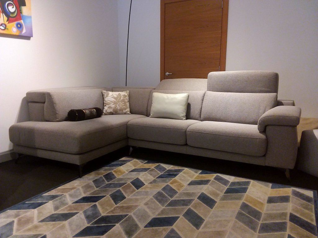 Sofá modular gris con cojines en una sala de estar, con una alfombra estampada y una puerta de madera.