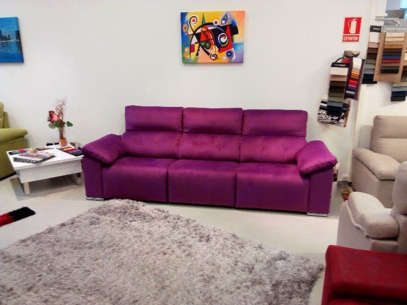 Sala de estar con un sofá morado, alfombra de pelo largo, sillón beige y coloridos cuadros en la pared.