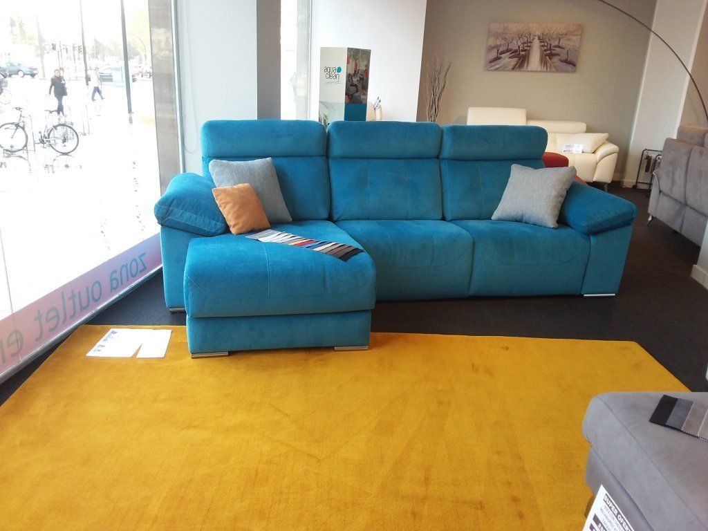 Luminoso salón con sofá modular turquesa, otomana y alfombra amarillo mostaza junto a la ventana.