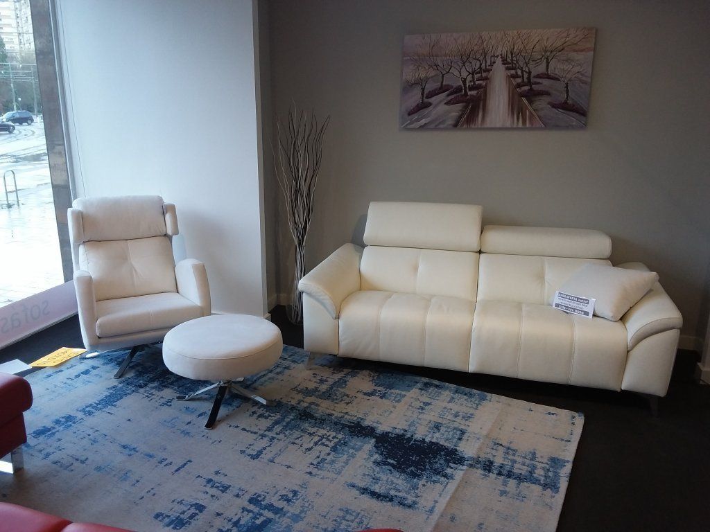 Sala de estar moderna con sofá y sillón blancos, otomana redonda, alfombra azul estampada y cuadros en la pared.