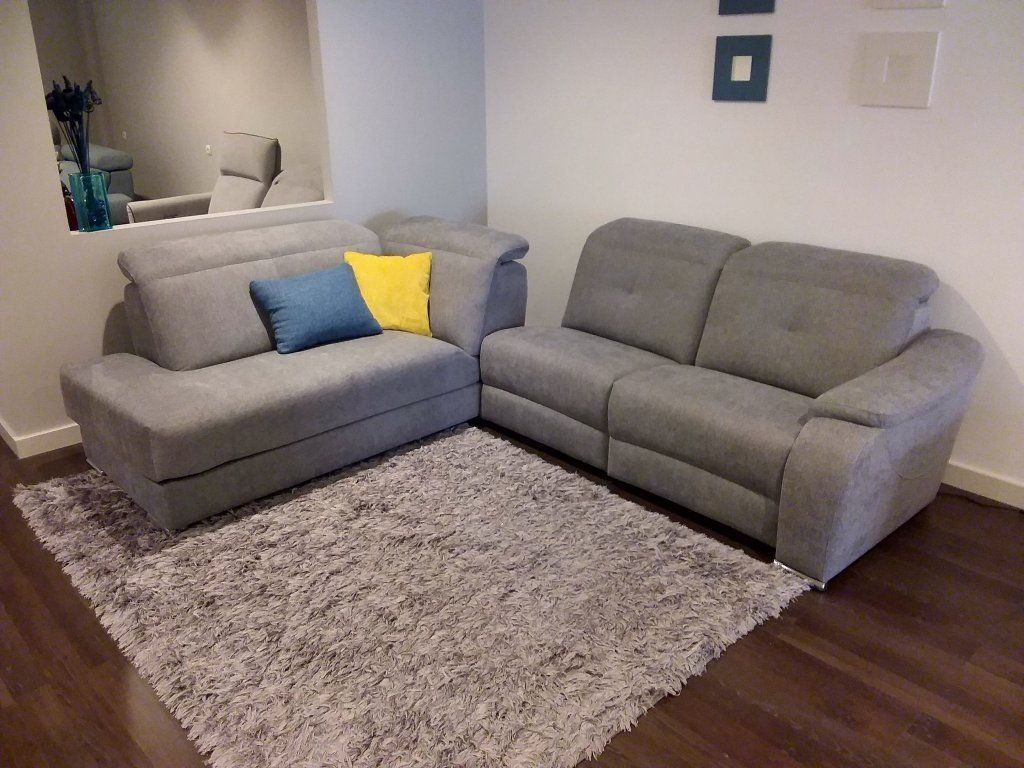 Sala de estar con dos sofás grises, cojines coloridos y una alfombra de pelo largo sobre suelo de madera oscura.