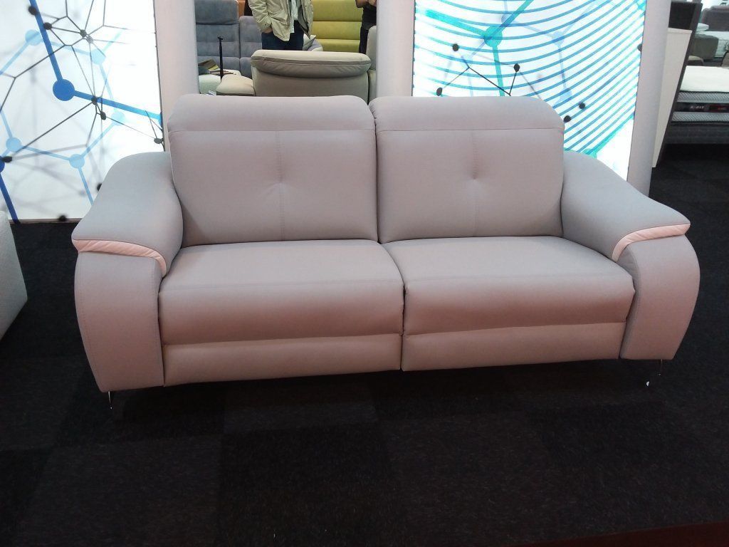 Sofá moderno de color rosa claro con brazos redondeados sobre un suelo negro en una sala de exposición.
