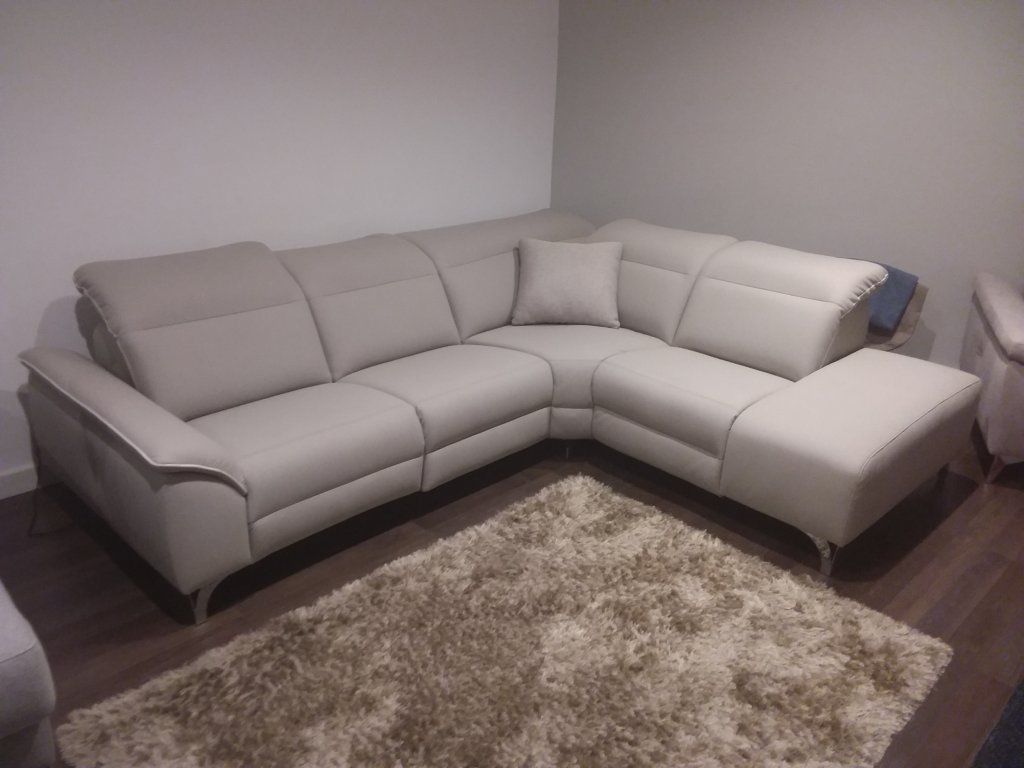 Sofá modular gris en un rincón de una habitación con una alfombra de pelo largo color beige sobre suelo de madera oscura.