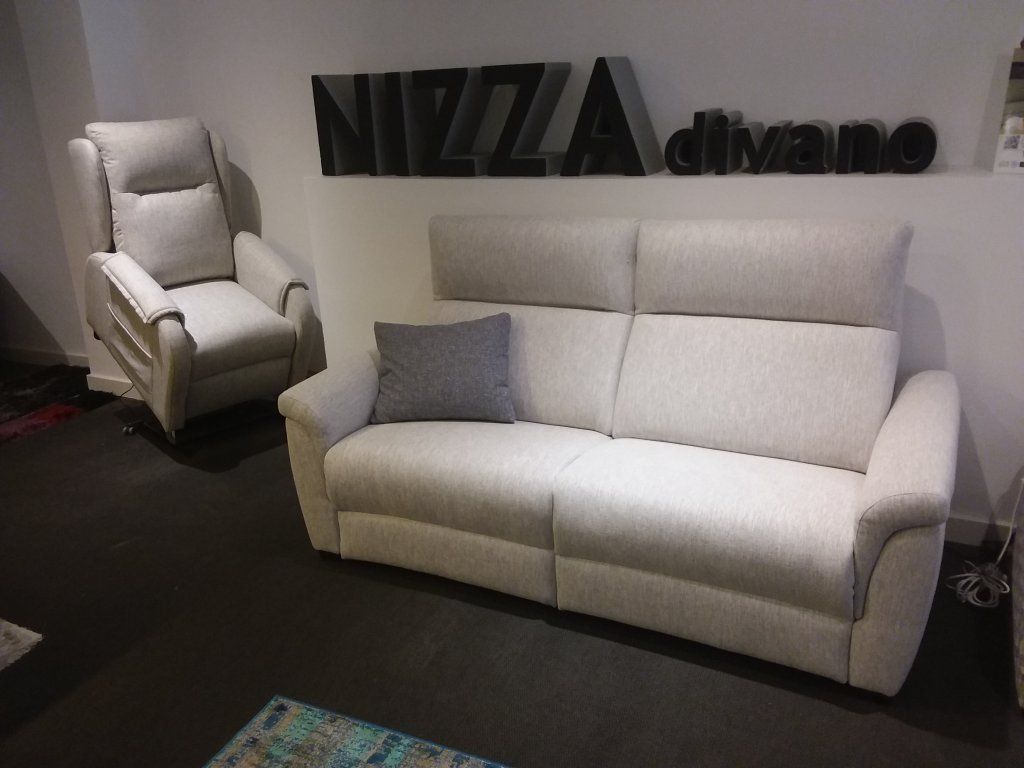 Sala de exposición con un sofá blanco y un sillón a juego sobre una alfombra oscura.