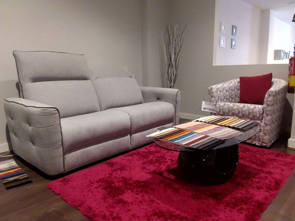 Sala de estar moderna con sofá gris, sillón estampado, mesa de centro y alfombra roja brillante.