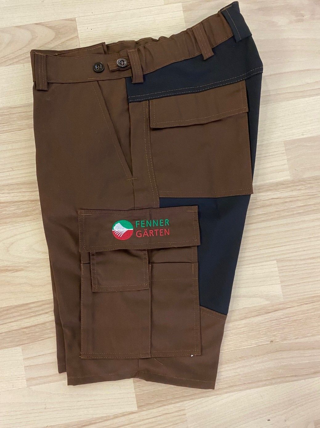 Ein Paar braun-schwarze Cargo-Shorts liegt auf einem Holzboden.