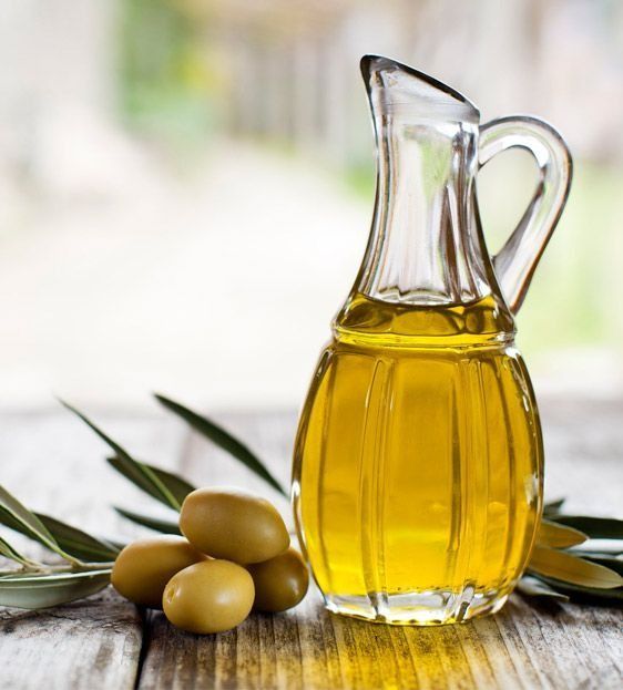 Una jarra de aceite de oliva reposa sobre una mesa de madera al lado de aceitunas.